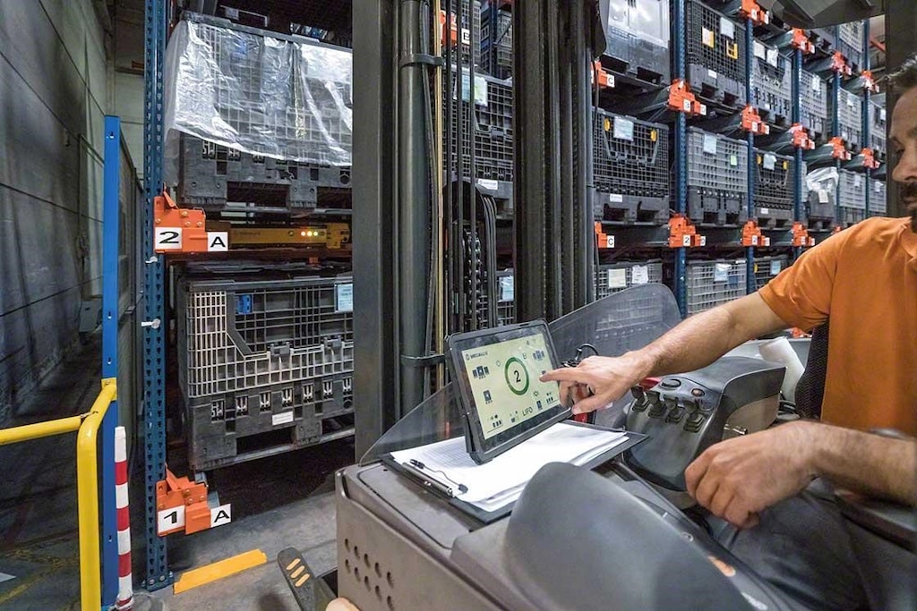 Um operador manuseia o Pallet Shuttle a partir da empilhadeira com um tablet digital em um armazém robotizado Um operador manuseia o Pallet Shuttle a partir da empilhadeira com um tablet digital em um armazém robotizado